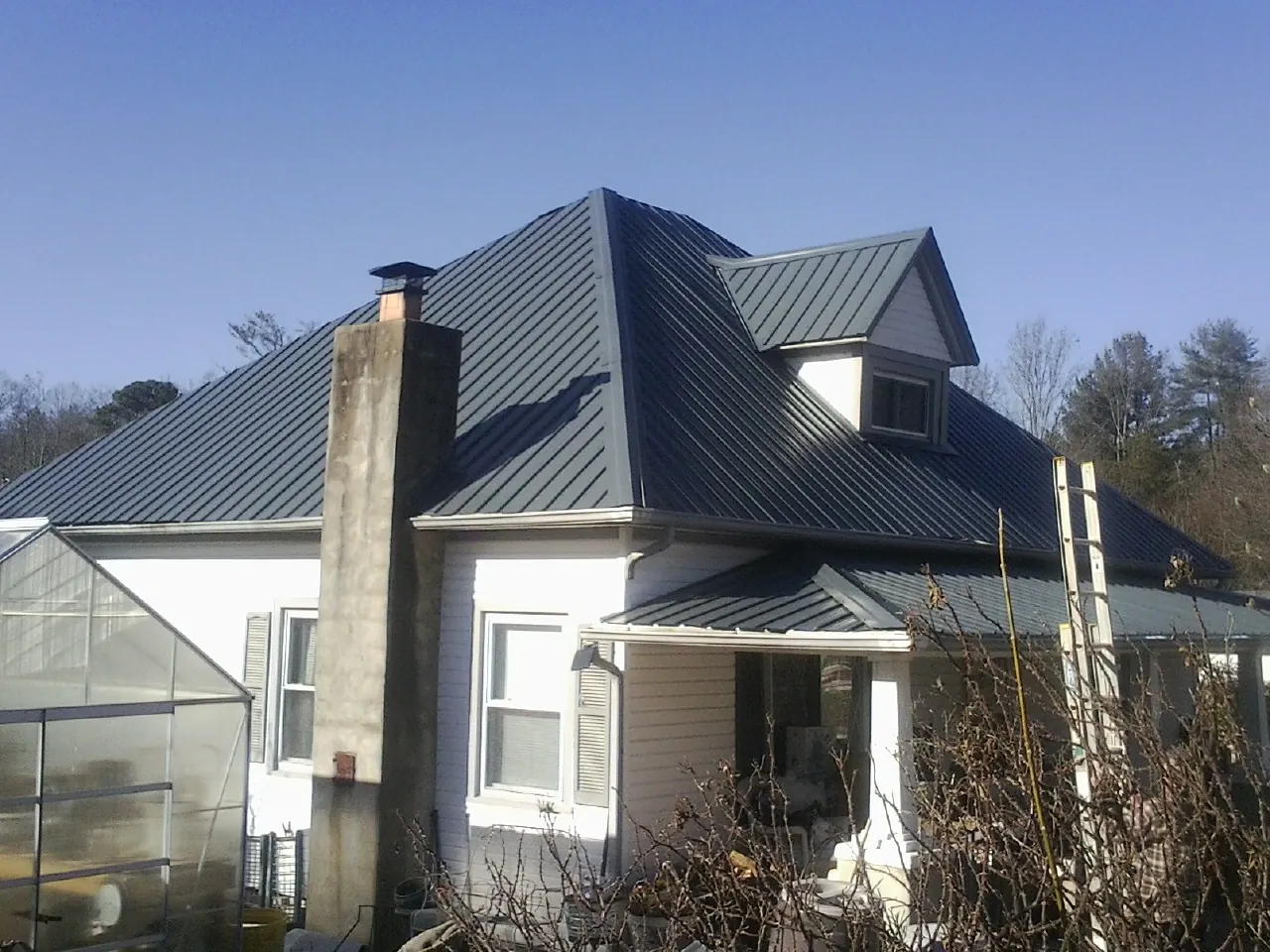Dark blue standing seam metal roof on a white farmhouse with dormer — Slate & Tile Roof Repair by Roofing Brothers in Grand Ridge