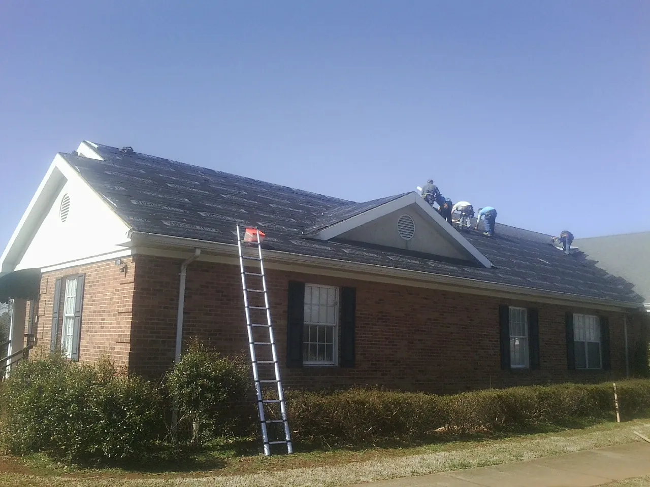 Crew tearing shingles off a brick ranch roof with a ladder set — Emergency Roof Repair work by our crew in Grand Ridge