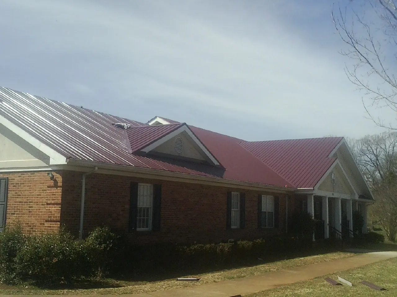 Red metal roof with gabled entries on a long brick building, from a Hail Damage Roof Repair job in Grand Ridge