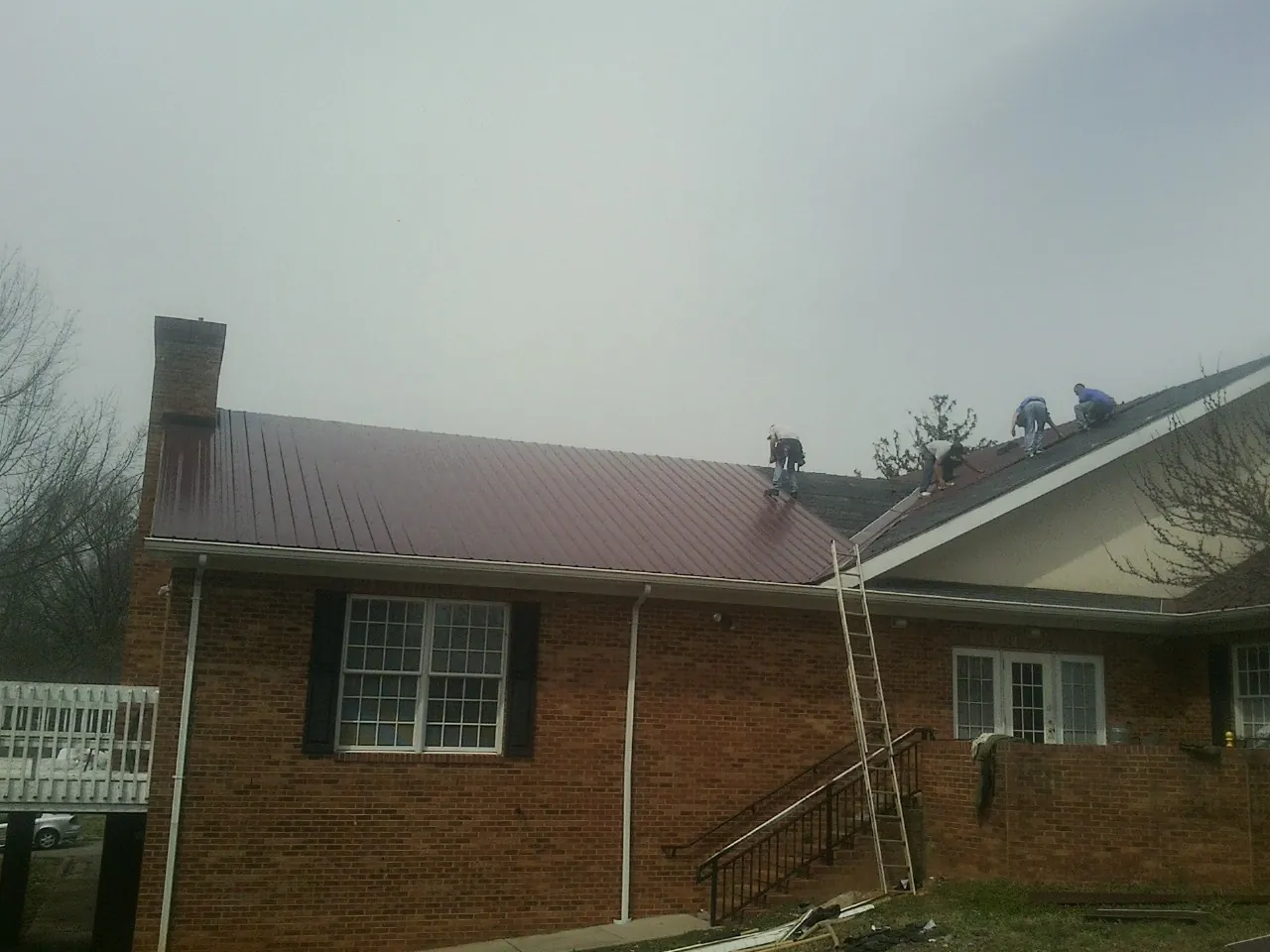 Crew setting red metal roofing panels on a brick home in Grand Ridge