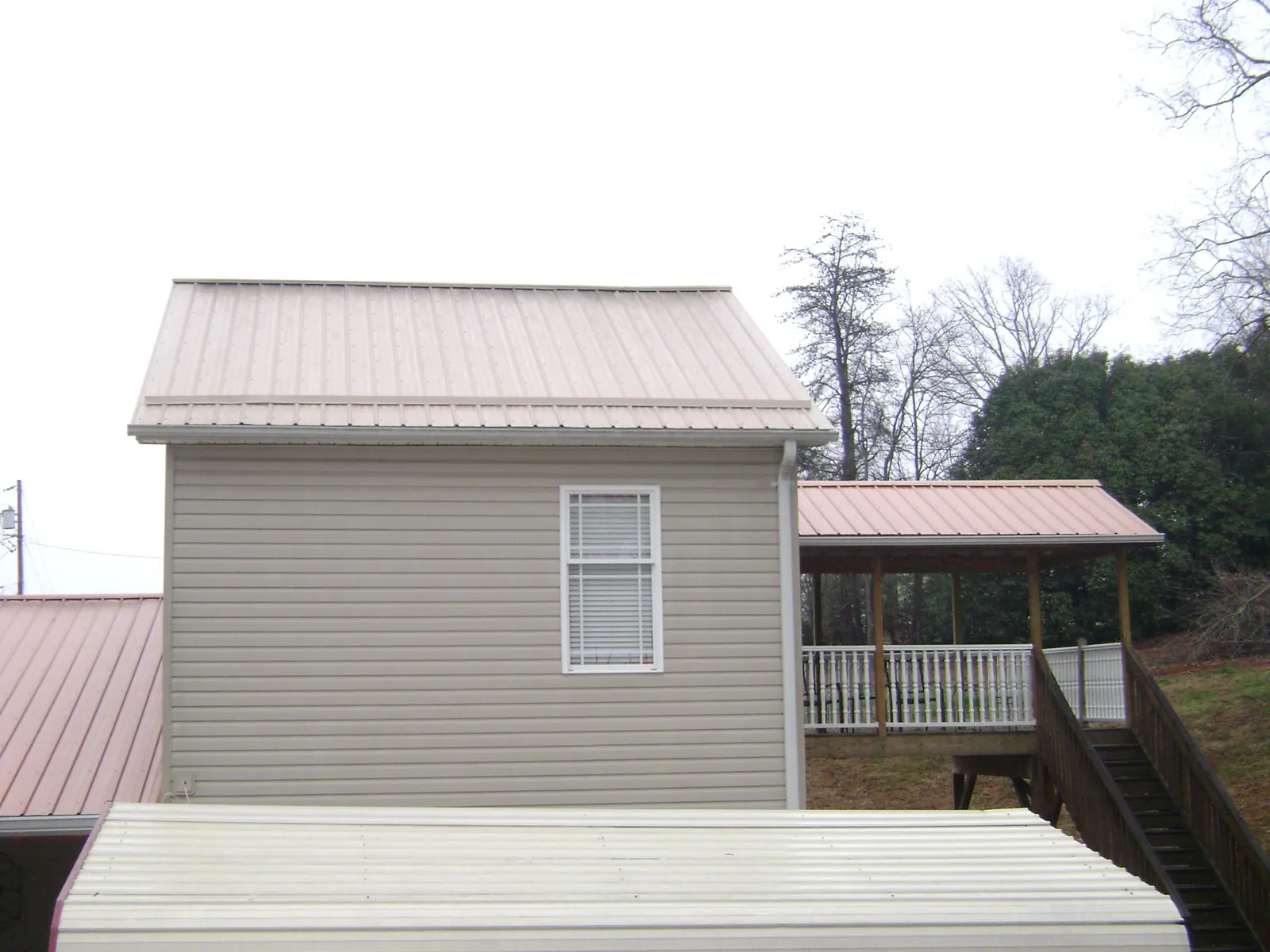 Tan metal roofs on a two story addition and attached porch, from a Roof Replacement job in Grand Ridge